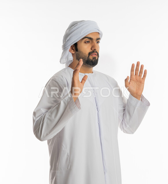 رفع اليدين بإيماءات التوقف وعدم الاقتراب، حماية النفس من ضرر خارجي, بورتريه من الجانب لرجل عربي خليجي إماراتي يرتدي الكندورة والعمامة يقف بحذر وذعر ورهبة, القلق والاحتياط والابتعاد عن شيء ما, خلفية بيضاء