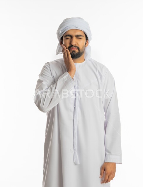 طلب العلاج والمساعده، تسوس الأضراس وإلتهاب اللثه، بورتريه لرجل عربي خليجي اماراتي يرتدي الكندورة الاماراتية والعمامة البيضاء يضع يده على خده بإيماءات تدل على الشعور بألم الأسنان، الحاجه لزيارة الطبيب، خلفية بيضاء
