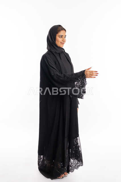 الوقوف لإلقاء التحيه والسلام, سيدة سعودية تقوم بالتعارف و الصداقه وتكوين علاقات, بورتريه من الجانب لشابة عربية خليجية إماراتية ترتدي العباءة السوداء تقوم بمد كفها للمصافحة، مفهوم الاستقبال والترحيب, صورة الجسم بالطول الكامل, خلفية بيضاء