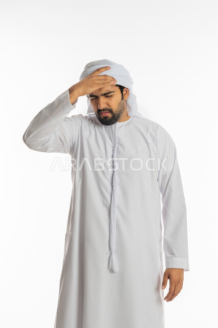 الشعور بالمرض وألم الرأس, آلام الشقيقة والصداع النصفي, الحاجة إلى العلاج والمساعده, بورتريه لرجل عربي خليجي إماراتي يرتدي الكندورة والعمامة يضع يديه على رأسه بإيماءات الانزعاج والتعب, خلفية بيضاء