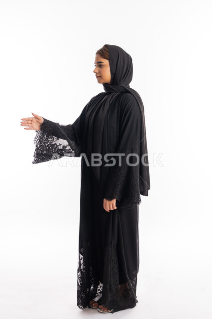 إلقاء التحيه والسلام, مفهوم الاستقبال والترحيب, سيدة سعودية تقوم بالتعارف و الصداقه وتكوين علاقات, بورتريه من الجانب لشابة عربية خليجية إماراتية ترتدي العباءة السوداء تقوم بمد كفها للمصافحة، صورة الجسم بالطول الكامل, خلفية بيضاء