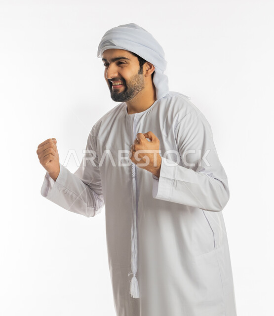 علامات وتعابير والفرح والقوة, الإعجاب والرضا و الشعور بالسعاده، تحقيق الاهداف و إنجاز المهام, بورتريه لرجل عربي خليجي اماراتي مبتسم  يرتدي العمامة والكندورة الاماراتية يرفع يديه بإيماءات النصر والفوز و الكسب, خلفية بيضاء
