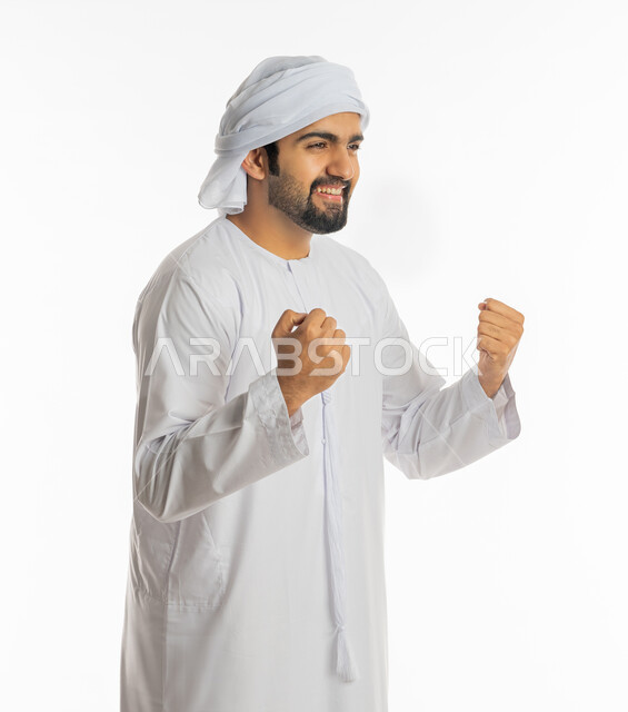 الإعجاب والرضا و الشعور بالسعاده، تحقيق الاهداف و إنجاز المهام, بورتريه لرجل عربي خليجي اماراتي مبتسم  يرتدي العمامة والكندورة الاماراتية يرفع يديه بإيماءات النصر والفوز و الكسب, علامات وتعابير والفرح والقوة, خلفية بيضاء