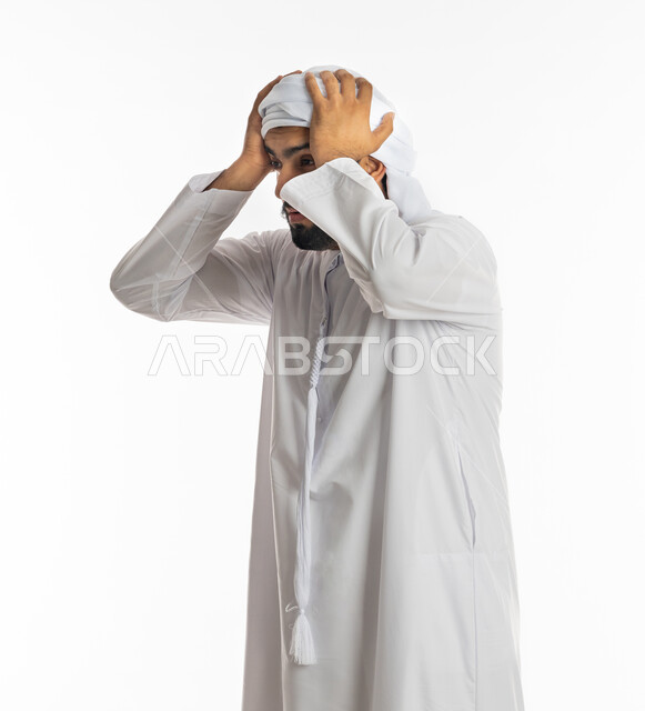 التفاجؤ والاستغراب من شيء ما, خسارة وفقدان شيء معين, الوقوف بإيماءات التعجب والدهشة، بورتريه من الجانب لشاب عربي خليجي إماراتي يرتدي الكندورة والعمامة الاماراتية يرفع يديه على رأسه بتعابير الصدمة والذهول، الانبهار وعدم تصديق أمر ما, خلفية بيضاء
