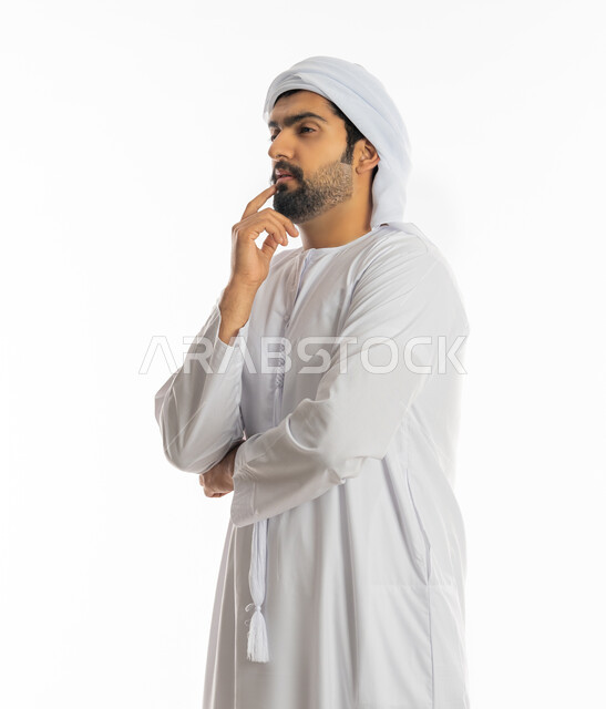 Absent-mindedness and focused decision-making, thinking and trying to find a solution to problems, looking carefully and planning for the future, portrait from the side of an Arab Gulf Emirati young man wearing a turban and kandora looking at something, white background