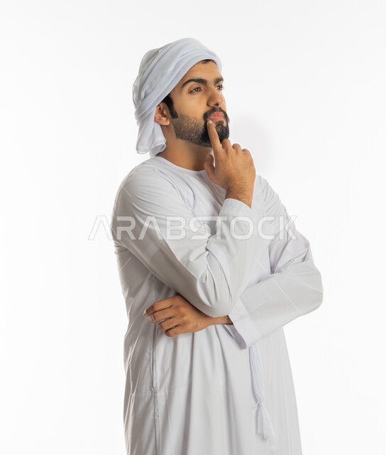 Looking carefully and planning for the future, thinking and trying to find a solution to problems, absent-mindedness and making decisions with focus, portrait of a young Arab Gulf Emirati man wearing a turban and kandora looking at something, white background