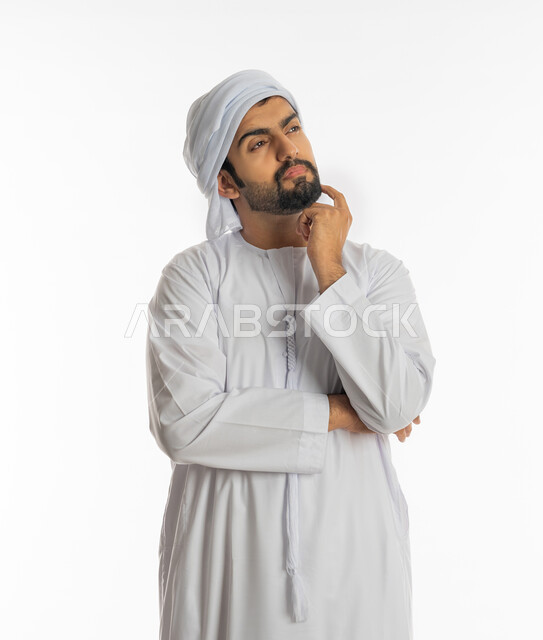 Thinking and trying to find a solution to problems, looking carefully and planning for the future, absent-mindedness and making decisions with concentration, portrait of a young Arab Gulf Emirati man wearing a turban and kandora looking at something, white background