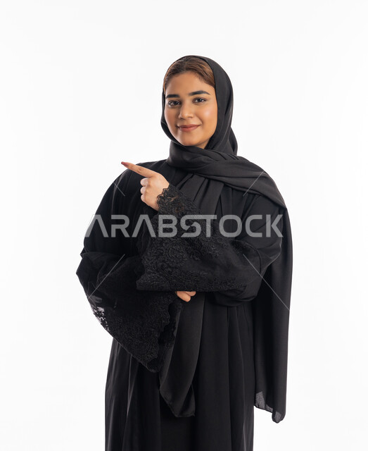 تعابير التأكد و تحديد مكان معين, الاشارة إلى شيء ما، سيدة سعودية تنظر إلى الكاميرا بإيماءات السرور, بورتريه لامرأة عربيه خليجيه إماراتية مبتسمة ترتدي العباءة السوداء ترفع اصبعها السبابة لاختيار أمر ما, خلفية بيضاء