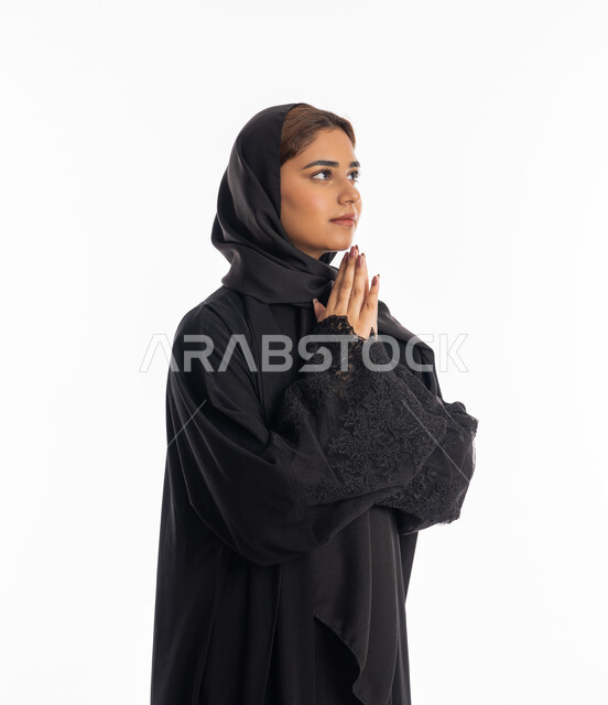التضرع إلى الله تعالى, طلب العون والرغبة في تحقيق الأمنيات, الدعاء والتوسل والاسترحام, الطلب بترجي وتذلل من رب العباد, بورتريه من الجانب لشابة عربية خليجية اماراتية ترتدي العباءة السوداء تنظر إلى الأعلى, سيدة سعودية ترفع يديها بخشوع واستعطاف, خلفية بيضاء
