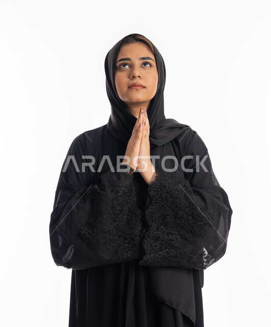 الوقوف بإيماءات الدعاء والتوسل والاسترحام, الطلب بترجي وتذلل من رب العباد, التضرع إلى الله تعالى, بورتريه لشابة عربية خليجية اماراتية ترتدي العباءة السوداء تنظر إلى الأعلى, سيدة سعودية ترفع يديها بخشوع واستعطاف, طلب العون والرغبة في تحقيق الأمنيات, خلفية بيضاء