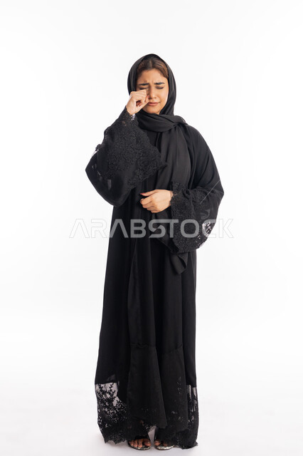 خسارة وفقدان شيء ما, الوقوف بتعابير الخيبة واليأس, سماع خبر حزين, الشعور بالهم والاكتئاب, بورتريه لشابة عربية خليجية إماراتية ترتدي العباءة السوداء تبكي وتضع يديها على عينيها بحزن, سيدة سعودية تقف بإيماءات البكاء والقهر, صورة الجسم بالطول الكامل, خلفية بيضاء