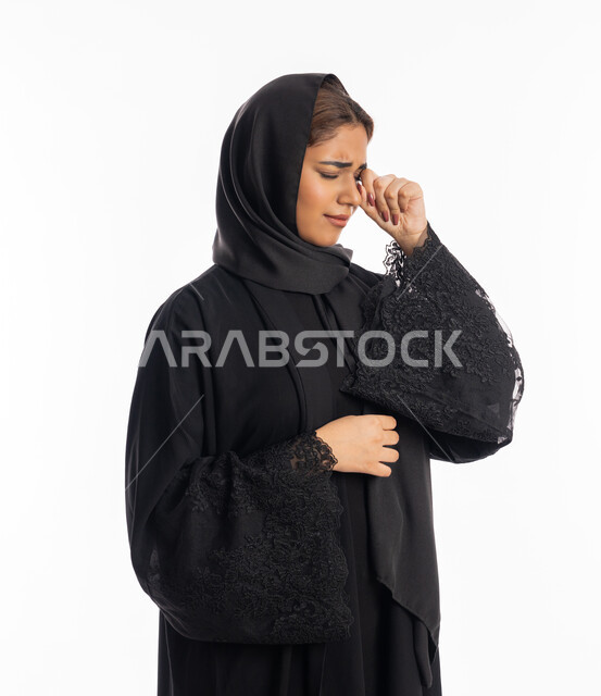 الوقوف بتعابير الخيبة واليأس, سماع خبر حزين, الشعور بالهم والاكتئاب, بورتريه مقرب لشابة عربية خليجية إماراتية ترتدي العباءة السوداء تضع يديها على عينيها بحزن, فقدان وخسارة شيء ما, سيدة سعودية تقف بإيماءات البكاء والقهر, خلفية بيضاء