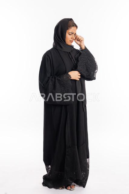 سماع خبر حزين, الشعور بالهم والاكتئاب, بورتريه لشابة عربية خليجية إماراتية ترتدي العباءة السوداء تضع يديها على عينيها بحزن, فقدان وخسارة شيء ما, سيدة سعودية تقف بإيماءات البكاء والقهر, صورة الجسم بالطول الكامل, خلفية بيضاء