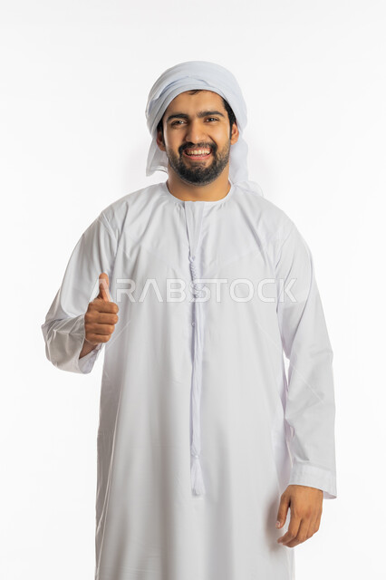 الوقوف بسرور وبشاشة وسعادة, الموافقة والرضا و القبول، التعبير عن الجودة والاتقان، بورتريه لشاب عربي خليجي إماراتي يرتدي الكندورة والعمامة الاماراتية يرفع يديه بإيماءات الجودة والامتياز والتميز، خلفية بيضاء