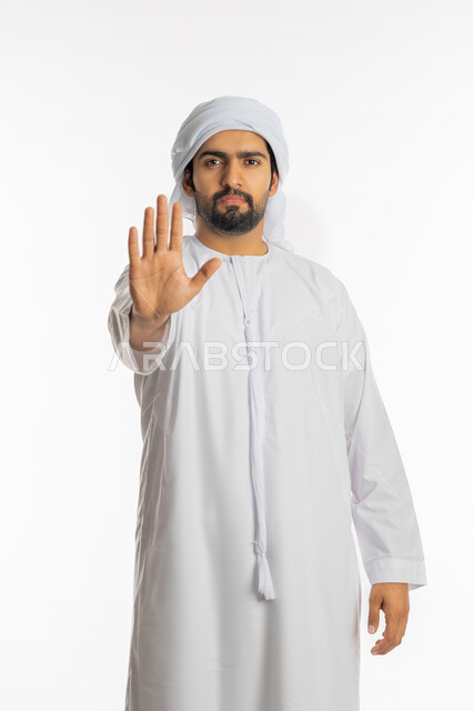 التهديد وطلب خفض الصوت, النهي عن فعل شيء ما, الصمت والتوقف عن الكلام, بورتريه لرجل عربي خليجي اماراتي يرتدي الكندورة والعمامة الاماراتية ينظر إلى الكاميرا ويرفع كفه للأعلى بإيماءات الرفض وعدم الرضى والقبول, خلفية بيضاء