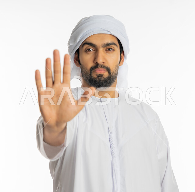 الصمت والتوقف عن الكلام, النهي عن فعل شيء ما,  بورتريه مقرب لرجل عربي خليجي اماراتي يرتدي الكندورة والعمامة الاماراتية ينظر إلى الكاميرا ويرفع كفه للأعلى بإيماءات الرفض وعدم الرضى والقبول, طلب خفض الصوت والتهديد, خلفية بيضاء