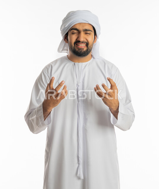 الحزن وطلب التوقف عن فعل الأخطاء, الوقوف بإيماءات العتاب والتوبيخ والرفض, محاولة ضبط النفس وكتم الغضب, بورتريه لشاب عربي خليجي إماراتي يرتدي الكندورة والعمامة الاماراتية يرفع يديه بانزعاج, خلفية بيضاء