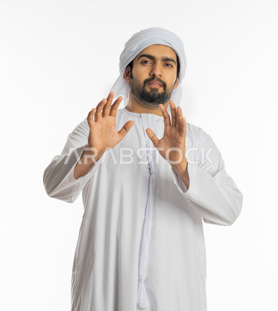 رفع اليدين بإيماءات التوقف وعدم الاقتراب, حماية النفس من ضرر خارجي, بورتريه لرجل عربي خليجي إماراتي يرتدي الكندورة والعمامة يقف بحذر وذعر ورهبة, القلق والاحتياط والابتعاد عن شيء ما, خلفية بيضاء