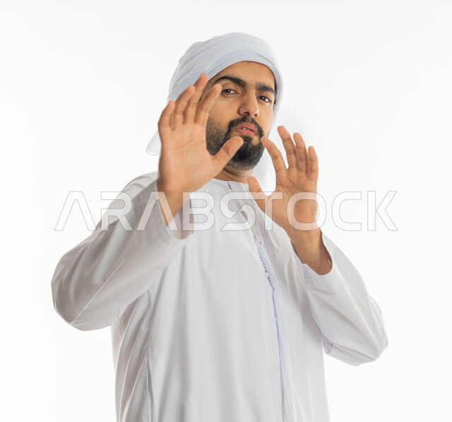 حماية النفس من ضرر خارجي, رفع اليدين بإيماءات التوقف وعدم الاقتراب, بورتريه مقرب لرجل عربي خليجي إماراتي يرتدي الكندورة والعمامة يقف بحذر وذعر ورهبة, القلق والاحتياط والابتعاد عن شيء ما, خلفية بيضاء