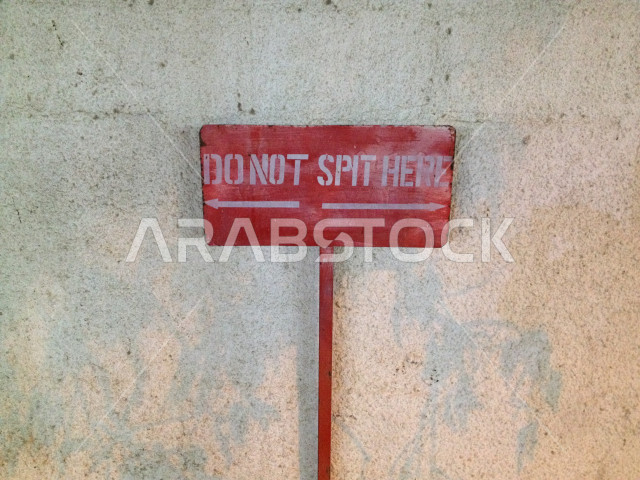 لافته حمراء وضعت بالقرب من جدار أبيض تمنع الناس من البصق هنا , لاتبصق هنا , عادات سيئة . 