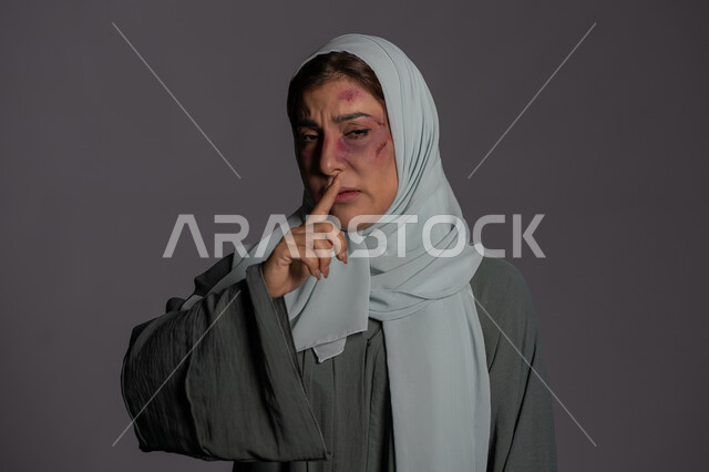 حقوق المرأة المسلمه, اليوم العالمي للقضاء على العنف ضد النساء 25 نوفمبر, سيدة سعودية حزينة, إجبار الامرأة على السكوت من قبل الرجال, العلاقات الزوجية الفاشلة, بورتريه مقرب لشابة عربيه إماراتية خليجية محجبة تضع اصبعها على فمها تنظر الى الكاميرا بإيماءات الصمت، خلفية رمادية