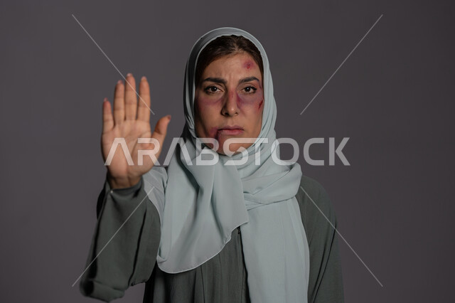 تعابير القوة و التعب, العلاقات الزوجية الفاشلة, 25 نوفمبر اليوم العالمي للقضاء على العنف ضد النساء ,حقوق المرأة المسلمه, آثار الكدمات الجسدية, بورتريه مقرب لشابة عربيه إماراتية خليجية محجبة ترفع كفها للاعلى بإيماءات طلب التوقف, سيدة سعودية حزينة, خلفية رمادية