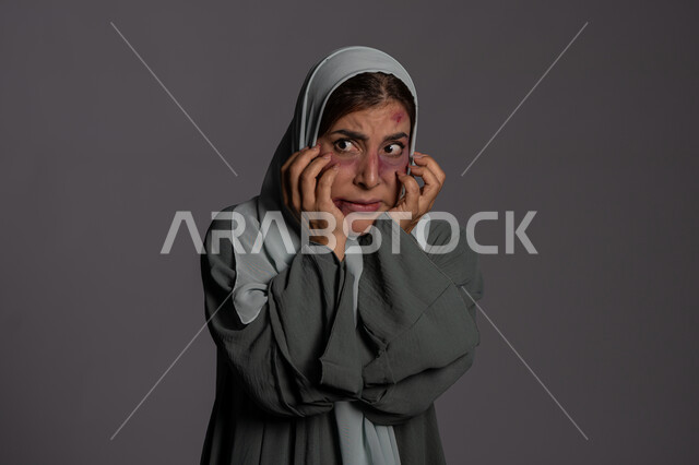 الامراض النفسية و المشاكل الزوجية, آثار الكدمات البدنية ,سيدة سعودية حزينة, اليوم العالمي للقضاء على العنف ضد النساء 25 نوفمبر, بورتريه مقرب لشابة عربيه إماراتية خليجية محجبة تضع يدها على وجهها وتنظر الى شيء ما بتعابير الذعر و الخوف, حقوق المرأة المسلمه، خلفية رمادية