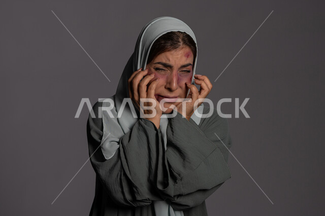 آثار الكدمات البدنية ,سيدة سعودية حزينة, اليوم العالمي للقضاء على العنف ضد النساء 25 نوفمبر, العلاقات الزوجية الفاشلة, بورتريه مقرب لشابة عربيه إماراتية خليجية محجبة تضع يدها على وجهها بتعابير الخوف و االبكاء و الذعر, حقوق المرأة المسلمه، خلفية رمادية