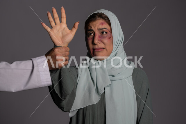 Preventing women from self-defense, failed marital relationships, November 25 International Day for the Elimination of Violence against Women, Muslim women being harmed by men, the effects of physical bruises, a close-up portrait of a veiled Emirati Gulf Arab young woman raising her hand up, a sad Saudi woman, gray background