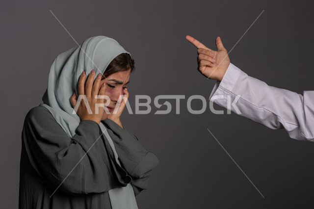 حقوق المرأة المسلمه، إيماءات التوبيخ والتنبيه، اليوم العالمي للقضاء على العنف ضد النساء 25 نوفمبر, إجبار الامرأة على السكوت من قبل الرجال, العلاقات الزوجية الفاشلة, بورتريه مقرب لشابة عربيه إماراتية خليجية محجبة تضع يدها على فمها بتعابير البكاء, سيدة سعودية حزينة, خلفية رمادية