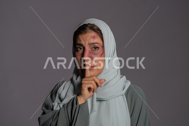 اليوم العالمي للقضاء على العنف ضد النساء 25 نوفمبر, سيدة سعودية حزينة, إجبار الامرأة على السكوت من قبل الرجال, العلاقات الزوجية الفاشلة, بورتريه مقرب لشابة عربيه إماراتية خليجية محجبة  تضع اصبعها على فمها تنظر الى الكاميرا بإيماءات الصمت, حقوق المرأة المسلمه، خلفية رمادية