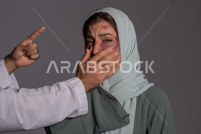 Forcing women to remain silent by men, expressions of reprimand and warning, International Day for the Elimination of Violence against Women, November 25, failed marital relations, close-up portrait of a veiled Arab Emirati Gulf woman looking with fearful gestures, a sad Saudi woman, Muslim women’s rights, gray background