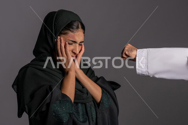 يد رجل مقبوضة بتعابير الضرب ,علاقات اسرية فاشلة, 25 نوفمبر اليوم العالمي للقضاء على العنف ضد النساء ,حقوق المرأة المسلمه ,آثار الكدمات البدنية, بورتريه مقرب لشابة عربيه إماراتية خليجية محجبة تتعرض للأذى الجسدي من قبل الرجال ,سيدة سعودية حزينة, خلفية رمادية