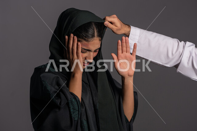 Defending the rights of Muslim women, failed family relationships, November 25, International Day for the Elimination of Violence against Women, exposure to physical harm by men, the effects of physical bruises, a close-up portrait of a veiled Arab Emirati Gulf woman raising her palm with an expression asking to stop, a sad Saudi woman, gray background