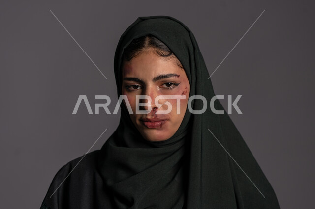 November 25, International Day for the Elimination of Violence against Women, Muslim women’s rights, the effects of physical bruises, failed marital relations, a close-up portrait of a veiled Arab-Emirati Gulf young woman looking at the camera with expressions of sadness and despair, a sad Saudi woman, gray background