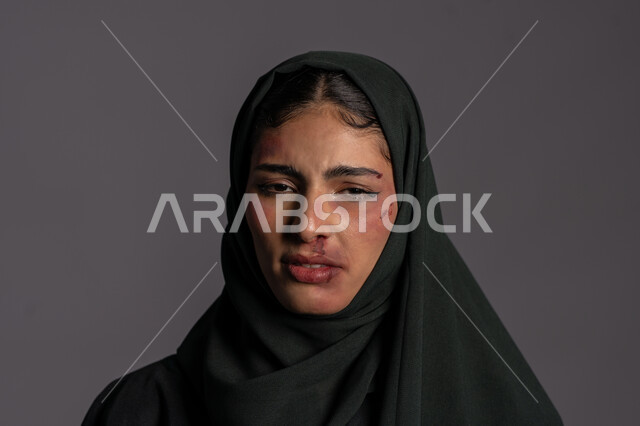 آثار الكدمات الجسدية ,العلاقات الزوجية الفاشلة, 25 نوفمبر اليوم العالمي للقضاء على العنف ضد النساء ,حقوق المرأة المسلمه, بورتريه مقرب لشابة عربيه إماراتية خليجية محجبة تنظر الى الكاميرا بتعابير الحزن و البكاء, سيدة سعودية حزينة, خلفية رمادية
