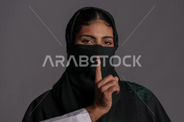 اليوم العالمي للقضاء على العنف ضد النساء 25 نوفمبر ,إجبار الامرأة على السكوت من قبل الرجال ,العلاقات الزوجية الفاشلة, بورتريه مقرب لشابة عربيه إماراتية خليجية محجبة تضع اللثام لإخفاء آثار الكدمات الجسدية, سيدة سعودية حزينة, حقوق المرأة المسلمه، خلفية رمادية