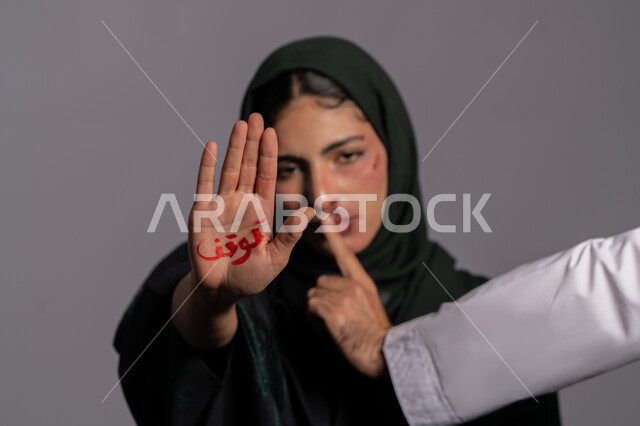 إجبار الامرأة على السكوت من قبل الرجال ,امراض نفسية ومشاكل زوجية, آثار الكدمات الجسدية, بورتريه مقرب لشابة عربيه إماراتية خليجية محجبة ترفع كفها للاعلى بعبارة توقف, 25 نوفمبر اليوم العالمي للقضاء على العنف ضد النساء ,سيدة سعودية حزينة, حقوق المرأة المسلمه، خلفية رمادية