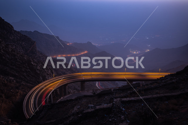 طريق جبلي منحني في الليل مع اضاءة السيارات , مسارات مضاءة في مدينة الطائف داخل المملكة العربية السعودية . 