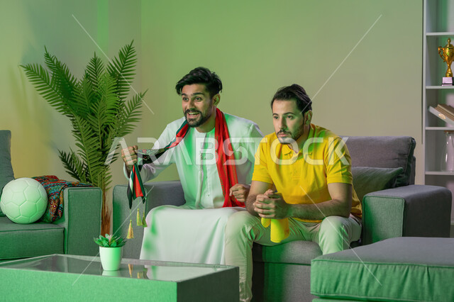 متعة مشاهدة المباراة مع الاصدقاء و المنافسة,   صديقان عربيان اماراتيان خليجيان يشاهدان مباراة للدوري العربي، شاب يشجع فريق و صديقه يشجع خصمه , ايماءات المنافسة والتحدي , أندية وتشجيع .