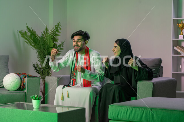 متابعة المباراة و دعم وتشجيع المنتخب العربي , زوجان عربيان خليجيان اماراتيان  يشاهدان  مباراة للدوري العربي في المنزل,  ايماءات وجه تدل على النصر , أندية وتشجيع .