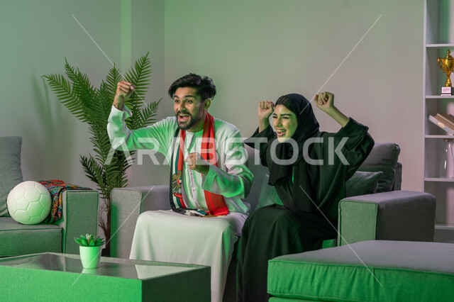 مشاهدة المباريات و تشجيع المنتخب العربي , اوشحة تشجيعية باللون الاحمر لكرة القدم, زوجان عربيان خليجيان اماراتيان  يشاهدان  مباراة للدوري العربي  ايماءات وجه تدل على النصر , أندية وتشجيع .