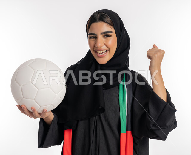 ارتداء وشاح تشجيع يحمل علم الإمارات، اهتمام الفتيات بمتابعة بالمباريات الرياضية، مشجعة للفرق والنوادي الوطنية، بورتريه لشابة عربية خليجية إماراتيه ترتدي العباية والحجاب تمسك بالكرة، فتاة سعودية تقوم برفع يدها بتعابير النصر والفوز، خلفية بيضاء