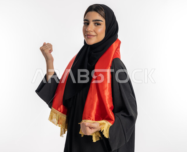 تشجيع للفرق الوطنية، النظر إلى الكاميرا بتعابير التحدي والقوة، اهتمام الفتيات بمتابعة المباريات، مفهوم تشجيع الفريق المفضل، بورتريه لشابة عربية خليجية إماراتيه ترتدي العباية والحجاب ووشاح باللون الأحمر، فتاة سعودية تقوم برفع يديها بإيماءات النصر، خلفية بيضاء