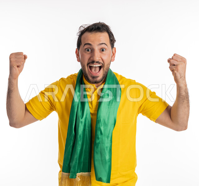 Passion for watching sports matches, looking at the camera with expressions of astonishment and astonishment, hand gestures indicating enthusiasm and strength, a supporter of national teams and clubs, a portrait of a young Arab Gulf Emirati man wearing a casual outfit and a green cheerleading scarf, a white background.