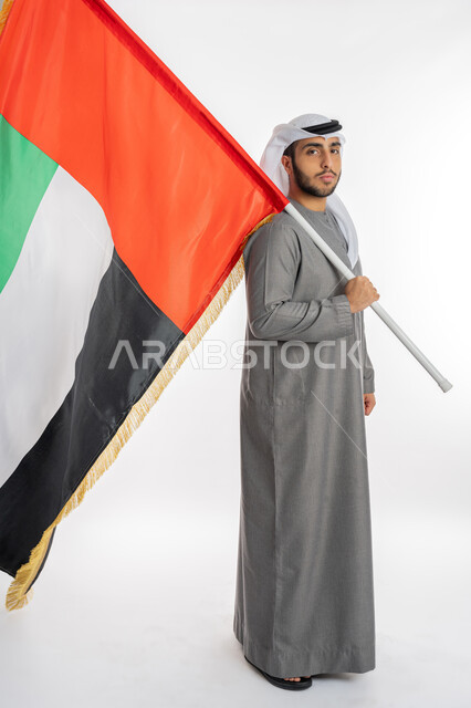 UAE Independence and Federation Day, December 2, portrait of a young Emirati Arab Gulf man wearing traditional clothing looking at the camera and holding the UAE flag in his hand, gestures of pride and pride in belonging to the homeland, celebrating UAE Flag Day November 3, white background, full length of the body