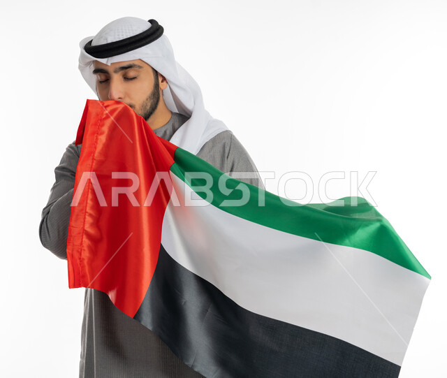 ذكرى يوم الاتحاد والاستقلال الإماراتي 2 ديسمبر، بورتريه لشاب إماراتي عربي خليجي يرتدي الزي التقليدي يحمل بيده علم دولة الإمارات ويقوم بتقبيله، الاحتفال بيوم العلم الإماراتي 3 نوفمبر، إيماءات الامتنان والإعجاب بالانتماء للوطن العربي، مناسبات وأعياد وطنية، خلفية بيضاء