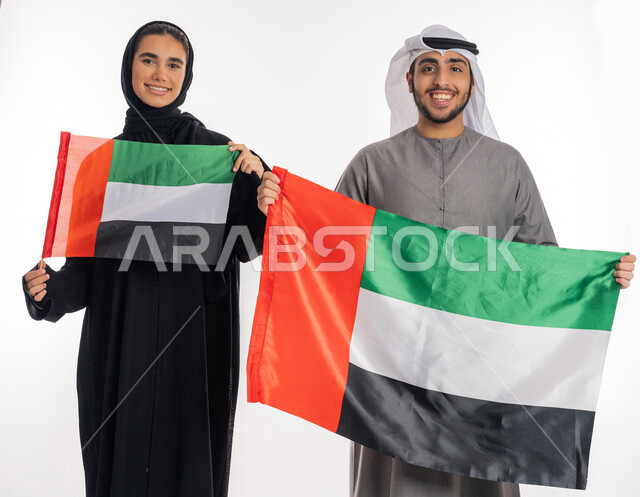 الاحتفال بيوم الاستقلال والاتحاد الإماراتي٢ ديسمبر، بورتريه لشاب وفتاة عربيان خليجيان إماراتيان مبتسمان يرتديان الزي التقليدي ويحمل كل منهما علم الإمارات بحجمين مختلفين، ذكرى يوم العلم الإماراتي ٣ نوفمبر، إيماءات الفرح السعادة بالانتماء للوطن العربي، خلفية بيضاء