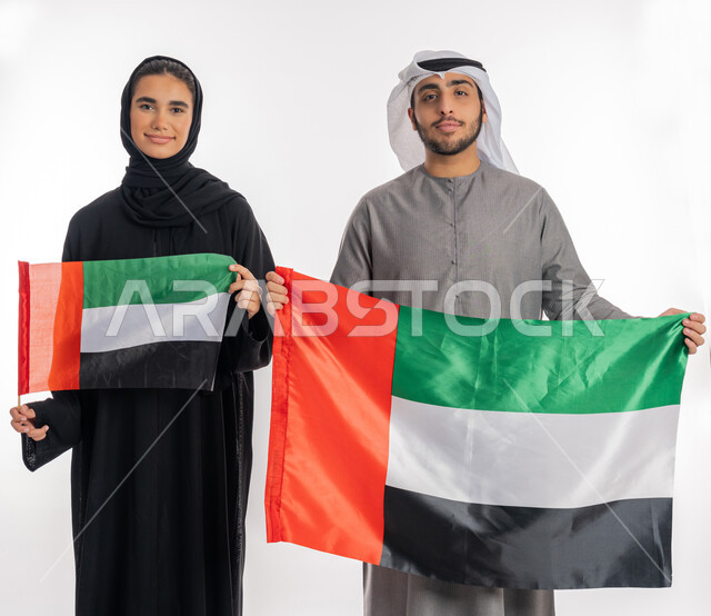 ذكرى يوم الاستقلال الإماراتي٢ ديسمبر، بورتريه لشاب وفتاة عربيان خليجيان إماراتيان مبتسمان يرتديان الزي التقليدي ويحمل كل منهما علم الإمارات بحجمين مختلفين، الاحتفال بيوم العلم الإماراتي ٣ نوفمبر، ايماءات الاعتزاز بالانتماء للوطن العربي، خلفية بيضاء