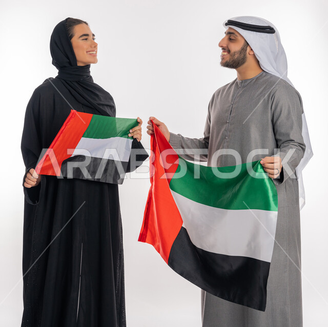 ذكرى يوم الاستقلال والاتحاد الإماراتي٢ ديسمبر، بورتريه لشاب وفتاة عربيان خليجيان إماراتيان مبتسمان يرتديان الزي التقليدي ينظران إلى بعضهما ويحملان بيديهما علم الإمارات، الاحتفال بيوم العلم الإماراتي٣ نوفمبر، الشعور بالفتخار والانتماء للوطن العربي، خلفية بيضاء
